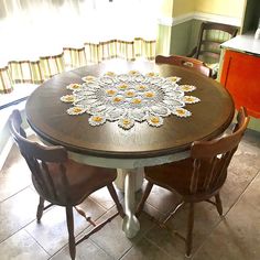 a dining room table with chairs and a doily on the table top in front of a window