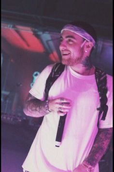 a man with long hair and piercings standing in front of a stage wearing a white t - shirt