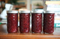 four jars filled with jam sitting on top of a wooden table next to a stack of books