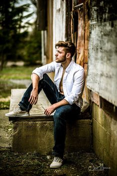 a man sitting on a bench in front of an old building wearing jeans and a white shirt