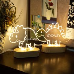 two light up dinosaurs sitting on top of a wooden table next to a vase with flowers