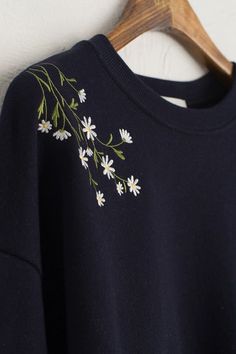 a black sweatshirt with white daisies embroidered on the front and back, hanging from a wooden hanger