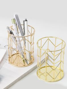 two gold pen holders with pens and pencils in them on top of a white table