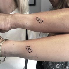 two women with matching tattoos on their arms, both have hearts tattooed on the arm