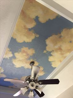 a ceiling fan with clouds painted on it in a room that is white and blue