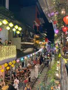 many people are walking down the railroad tracks at night time, with lanterns hanging above them