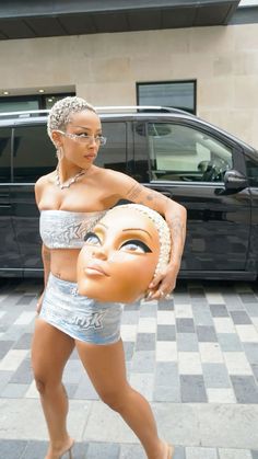 a woman is walking down the street with a fake face on her head and an orange mask in her hand