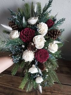 a bouquet of white and red flowers on top of a wooden table with pine cones