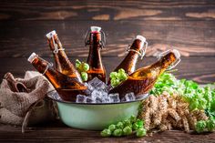 several bottles of beer are in an ice bucket on a wooden table with green hops