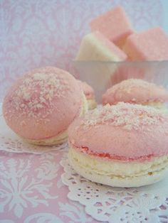 two pink macaroons sitting on top of a doily next to some sugar cubes