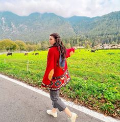 a woman is walking down the road in front of some mountains and cows on the other side