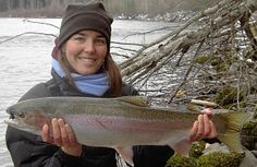 a woman holding a large fish in her hands near the water and snow covered ground