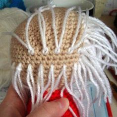 a hand holding a crocheted hat with fringes on it's head