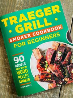 the book cover for trader grill smoker cookbook sits on a wooden table next to a fork and knife