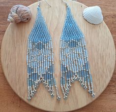 two pairs of beaded earrings sitting on top of a wooden table next to a seashell