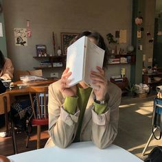 a person sitting at a table with a book in front of their face and hands