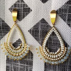 two pairs of beaded earrings hanging on a checkered wallpapered surface, one in gold and the other in white