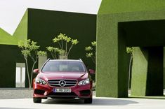 a red car is parked in front of some green plants and trees on the side of a building