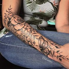 a woman sitting on the floor with her arm covered by flowers and leaves tattoo design