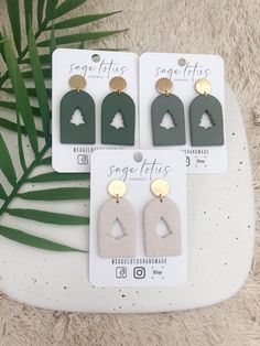 three pairs of earrings with trees on them sitting next to a palm leaf and white background