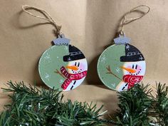 two snowman ornaments hanging from a tree with twine ribbons on it's ends