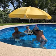 two men are in the pool under an umbrella