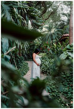 a pregnant woman standing in the middle of a jungle with trees and plants around her