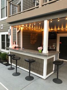 an outdoor bar with stools and lights on the side of it in front of a building