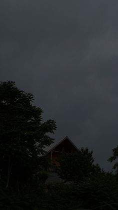 the sky is dark and gloomy with some trees in front of it on a cloudy day