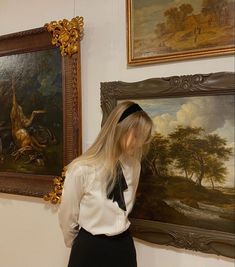 a woman is standing in front of paintings and looking at the wall with her hand on her hip