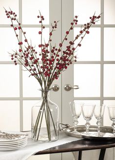 a vase filled with red berries sitting on top of a table next to wine glasses