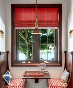 two chairs and a table in front of a window with red roman shades on the windowsill