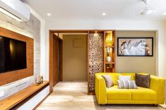 a living room with a yellow couch and television on the wall in front of it