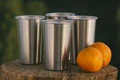 three silver cups sitting on top of a wooden stump next to an orange and another metal cup