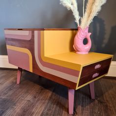 a pink vase sitting on top of a wooden table next to a yellow drawer with two feathers sticking out of it