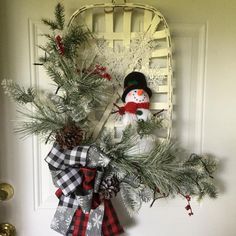 a snowman is hanging on the door with pine cones and evergreen branches in front of it