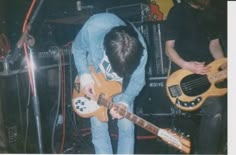 two young men playing guitars in front of microphones