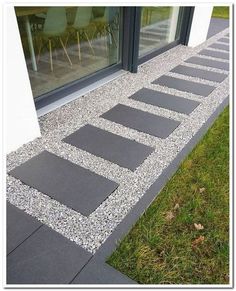 an outdoor walkway with stepping stones on the ground and grass in front of a glass window