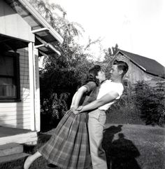 an old black and white photo of a man holding a woman in front of a house