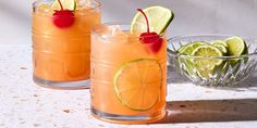 two glasses filled with drinks sitting on top of a table next to a bowl of limes