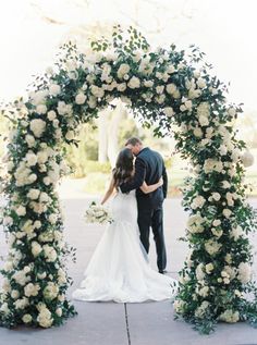 a bride and groom standing under an arch with white flowers