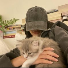 a woman holding a cat in her arms while wearing a baseball cap and hoodie