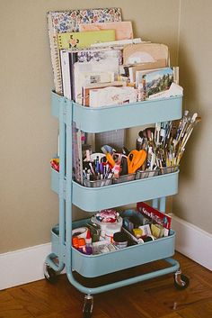 a blue cart filled with lots of crafting supplies on top of a hard wood floor