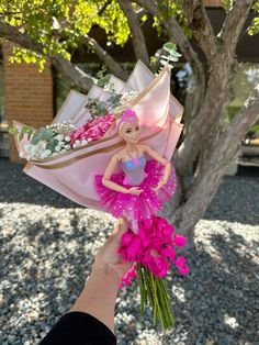 a hand holding a bouquet of flowers with a barbie doll in it's dress