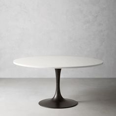 an oval white table with black legs on a concrete floor in front of a gray wall