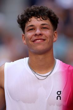 a young man wearing a white tank top smiles at the camera while standing in front of a crowd