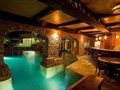 an indoor swimming pool surrounded by stone walls and flooring with lights on the ceiling