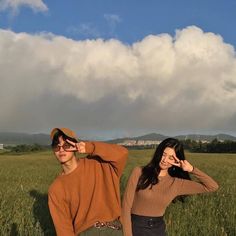 two people are standing in the grass with their hands on their ears and one is wearing a brown sweater