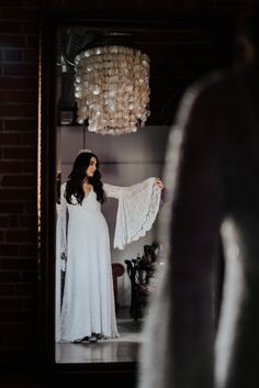 a woman standing in front of a mirror wearing a white dress and holding a lace shawl