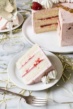 two slices of strawberry cake on plates with wine glasses and strawberries in the background